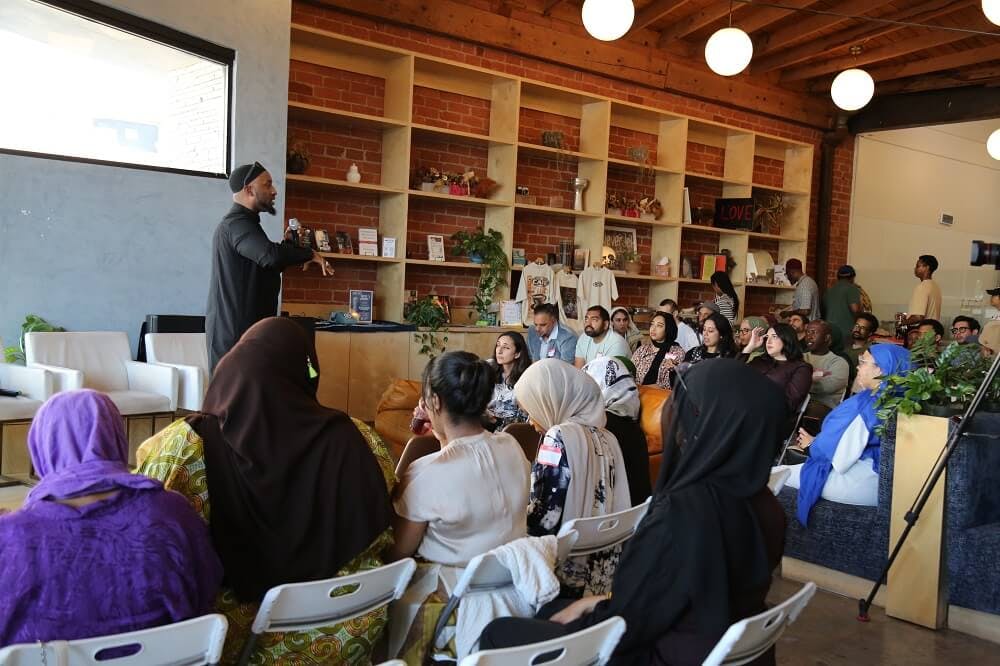 Person speaking to an audience in a room with shelves of items