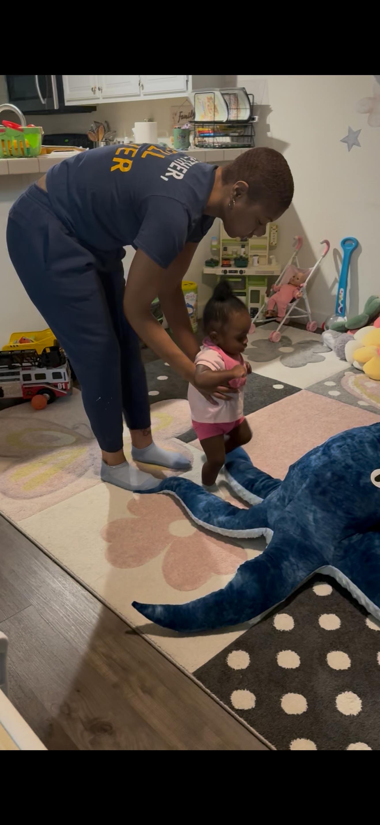 Person holding hands of a child learning to walk on a play mat