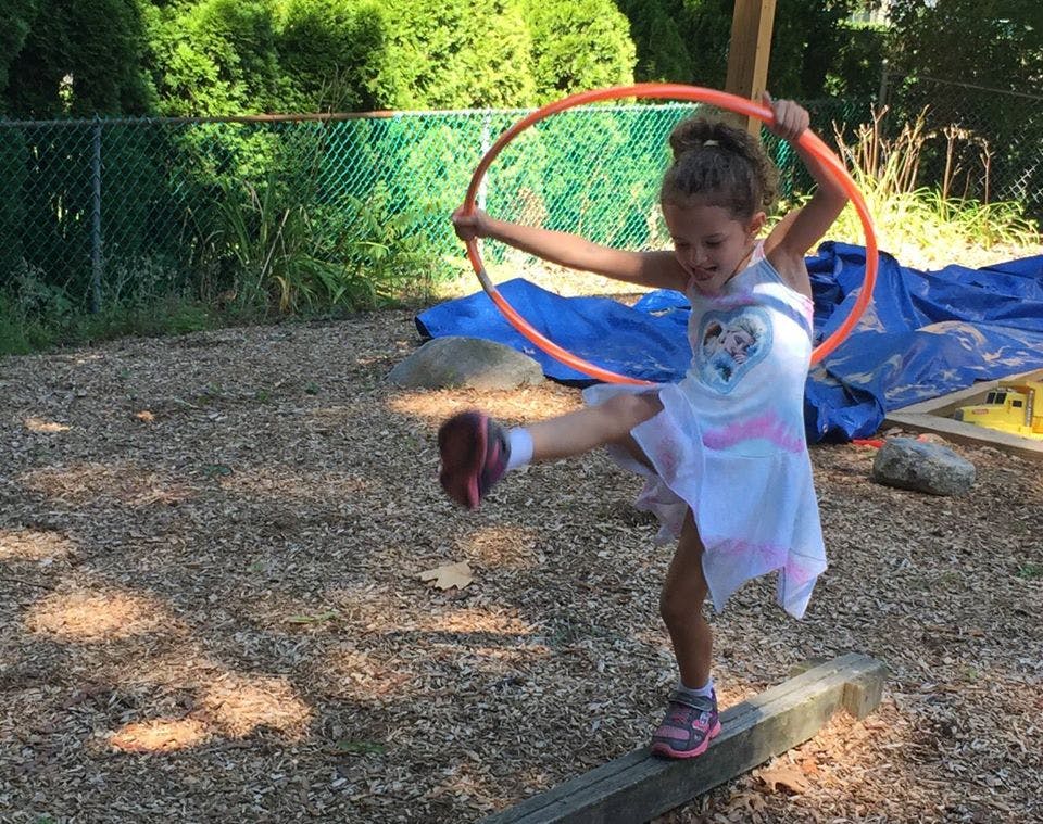 Child balancing on a wooden beam while holding a hula hoop