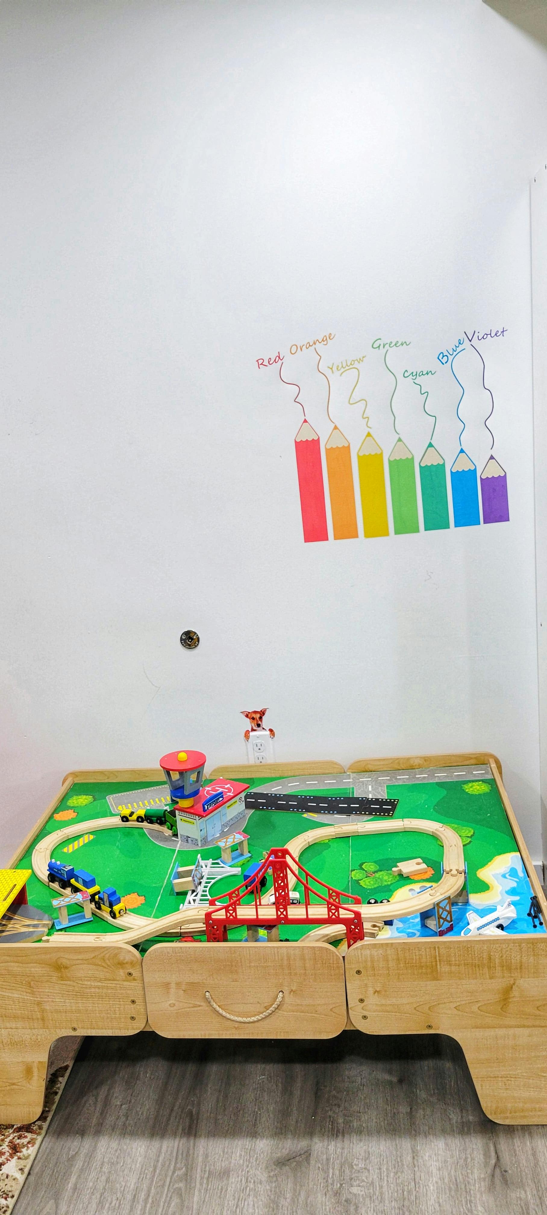 Play table with a toy train set and a wall decal of colored pencils