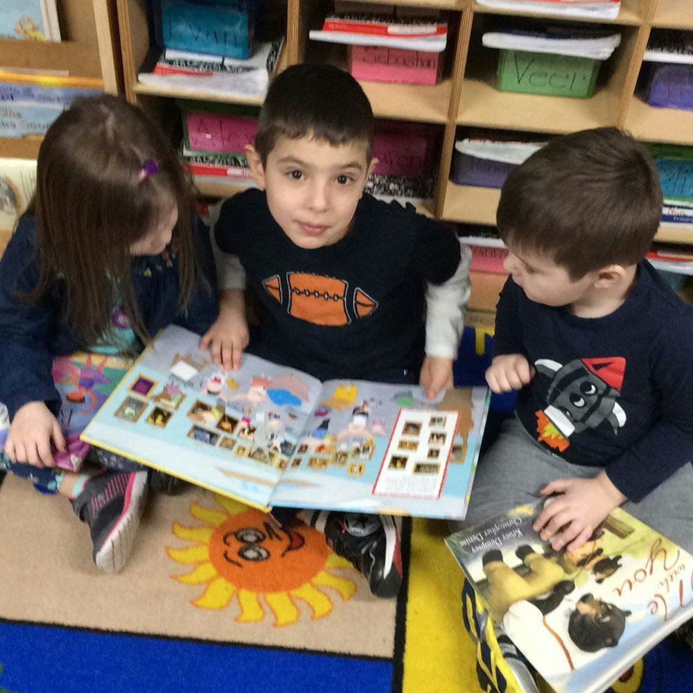 Three children looking at a book in a classroom