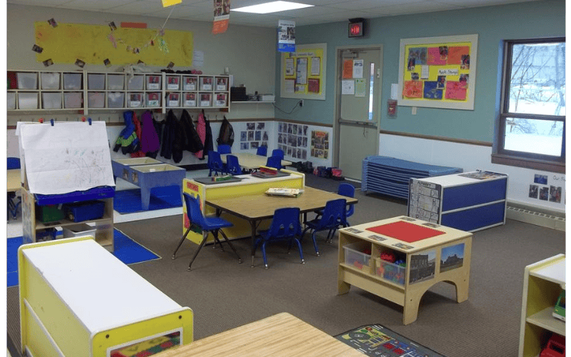 A colorful classroom with child-sized tables and chairs, an easel, and coat hooks