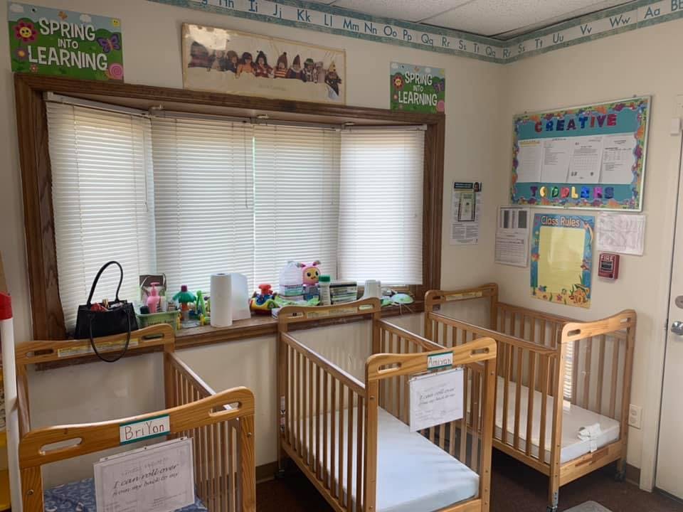 Three empty cribs in a room with a window and bulletin board