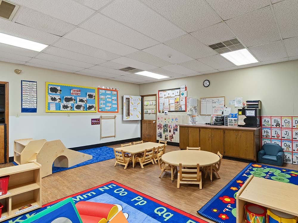 Classroom with small tables and chairs, play equipment, and colorful rugs