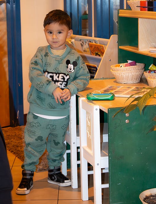 Child standing next to a small table in a classroom