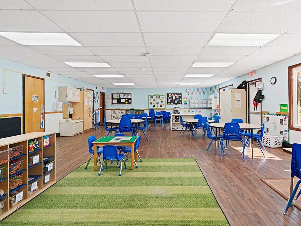 Classroom with small tables and chairs, a green striped rug, and toy storage