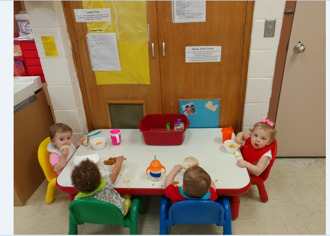 Four children eating at a small table in a classroom