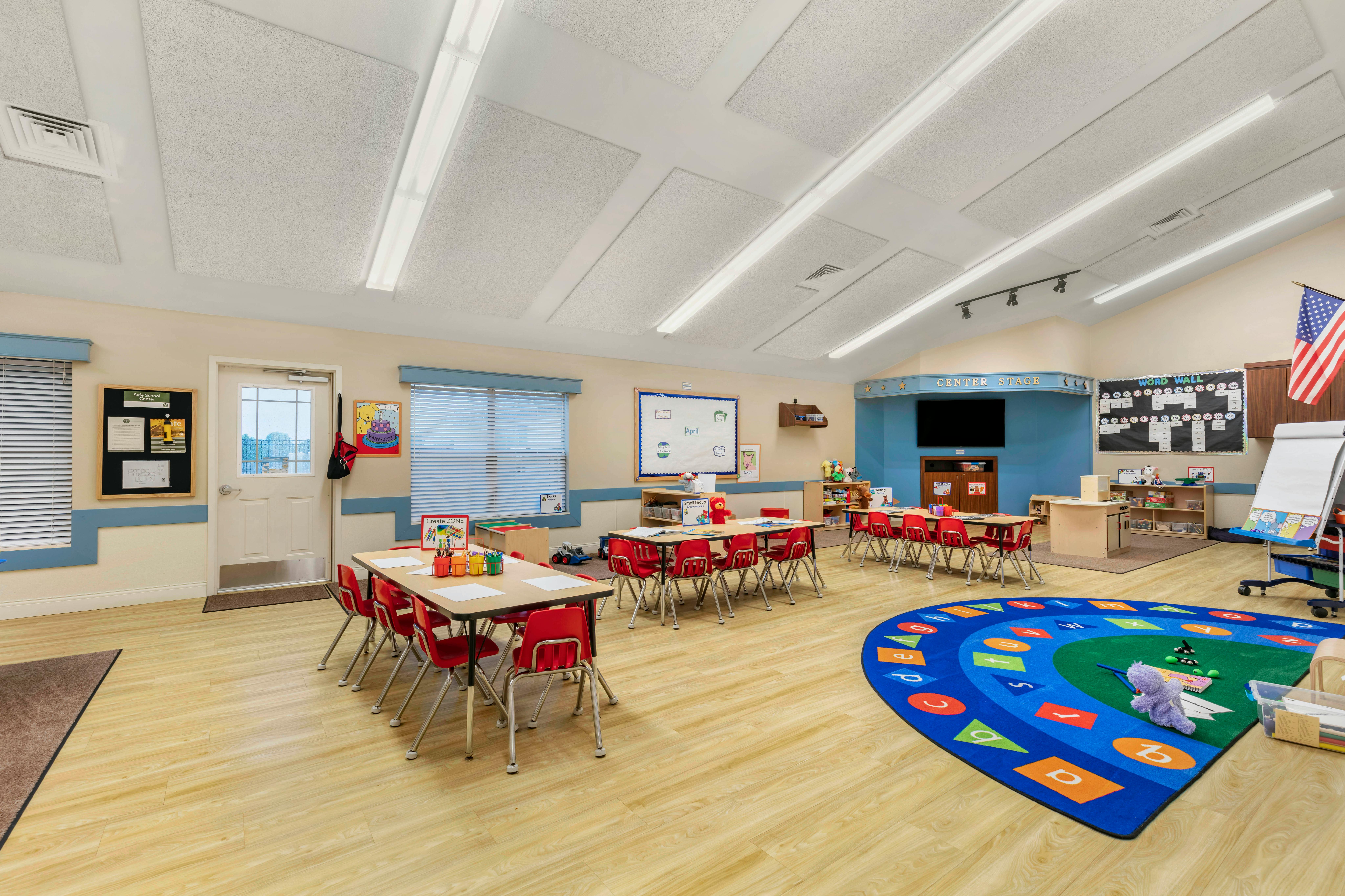 Empty classroom with small tables and chairs, a play rug, and activity areas