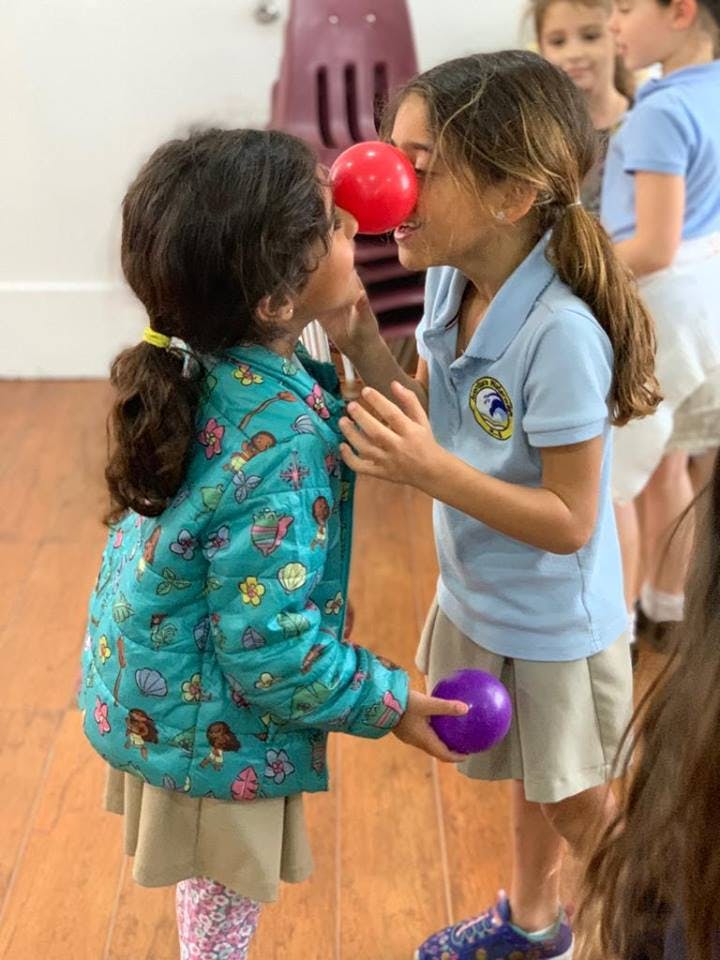 Two children balancing a red ball between their faces