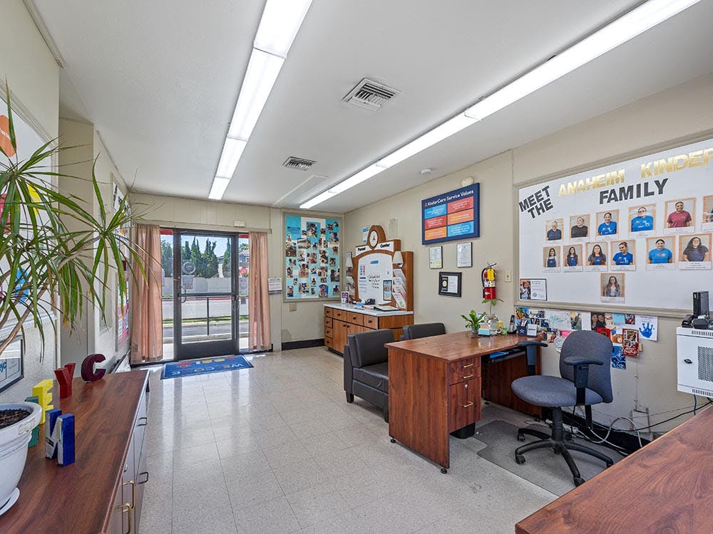Reception area with a desk, chairs, a plant, and a board displaying photos of people