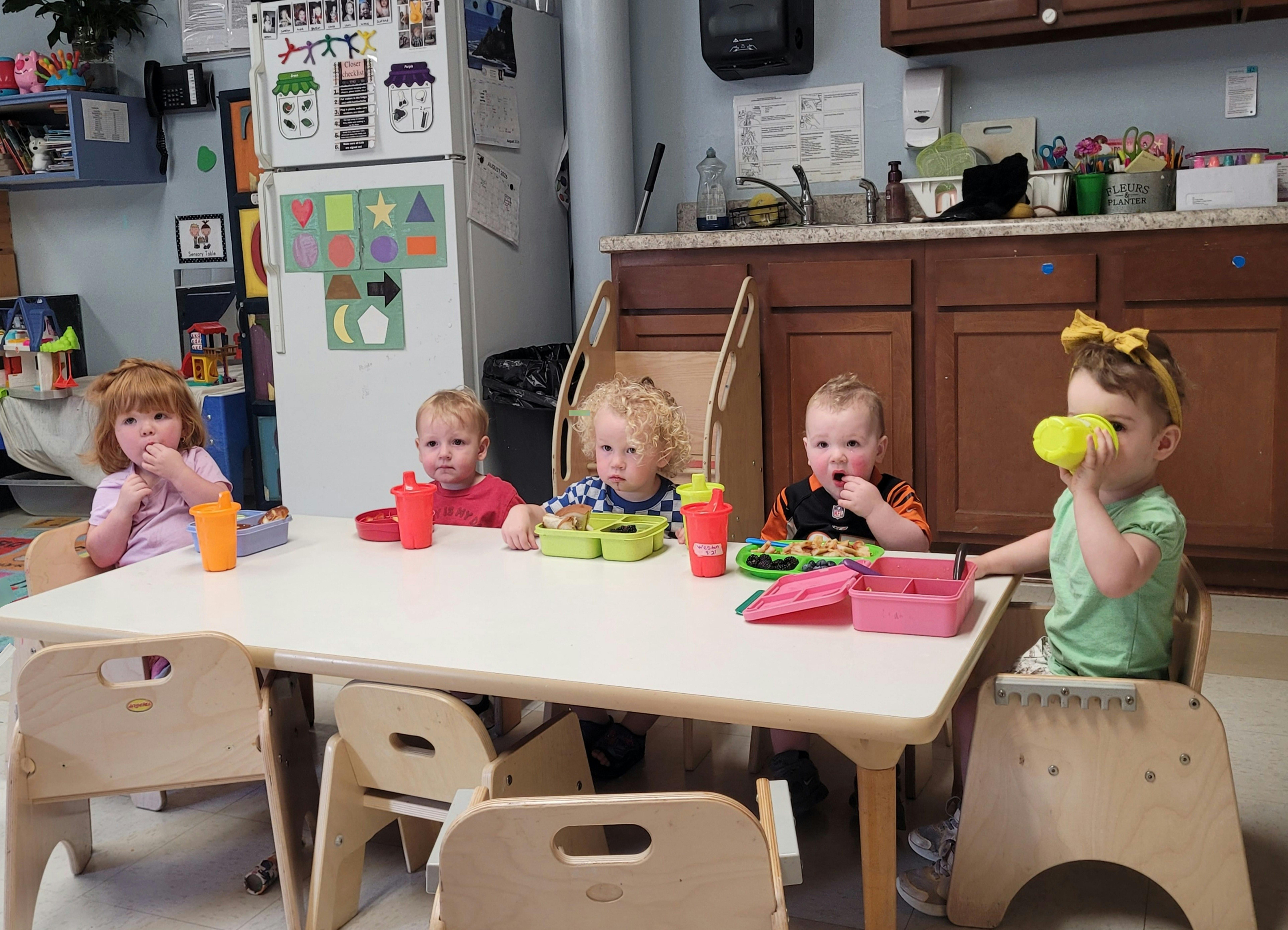 Five children eating lunch at a table in a classroom