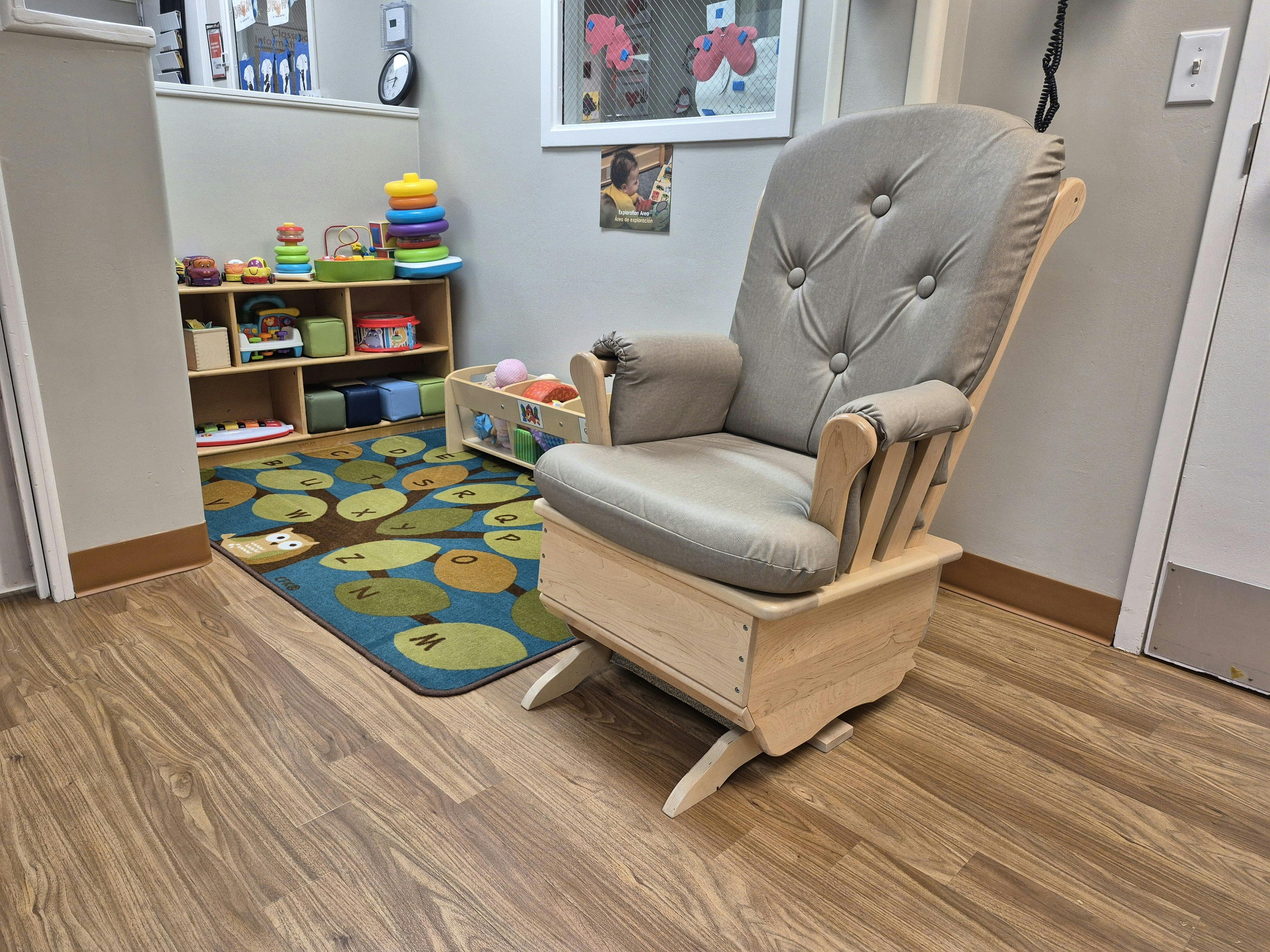 Glider chair with a rug and shelves of toys in a playroom