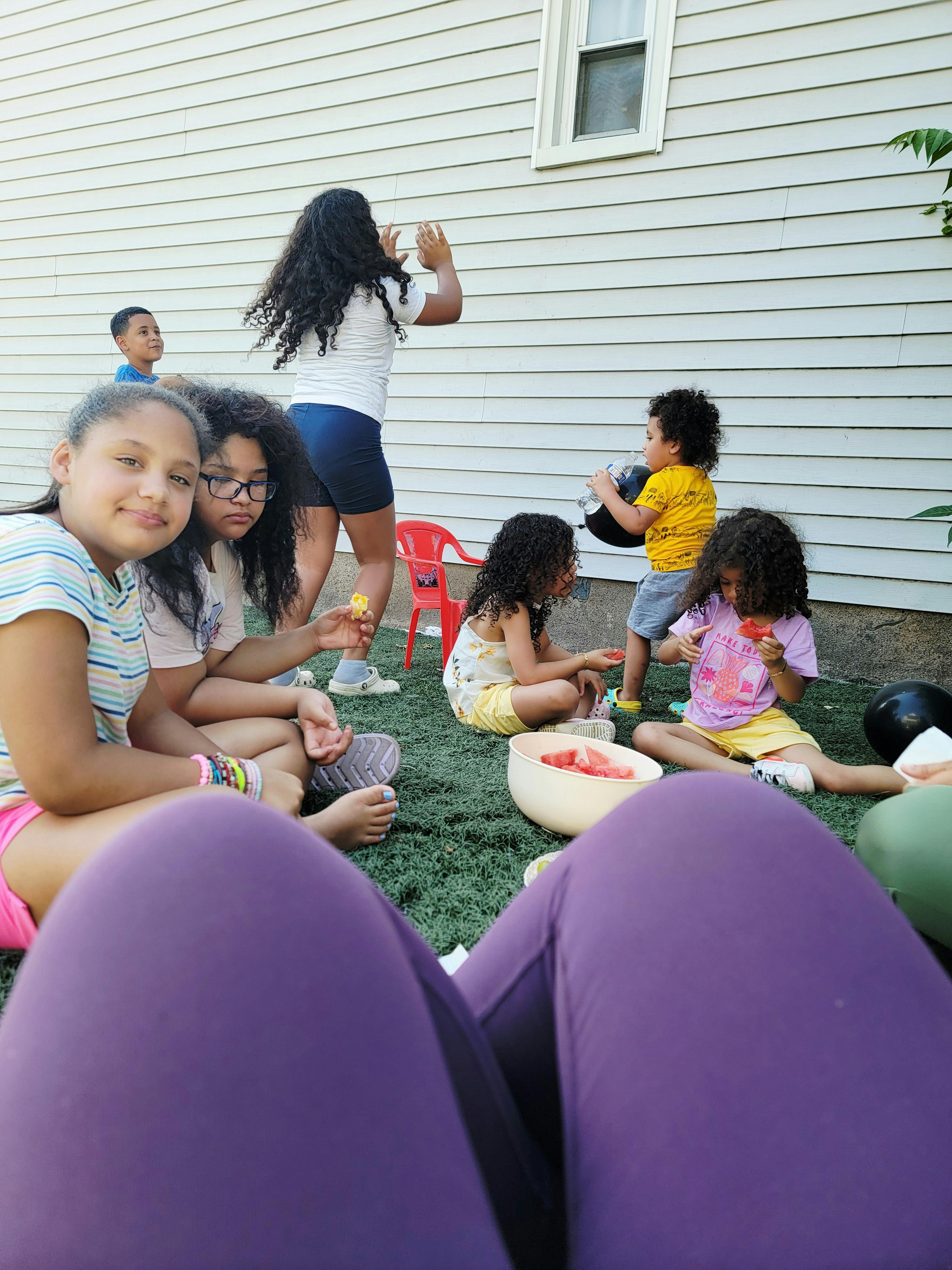 Children and adults gathered outdoors, some eating watermelon