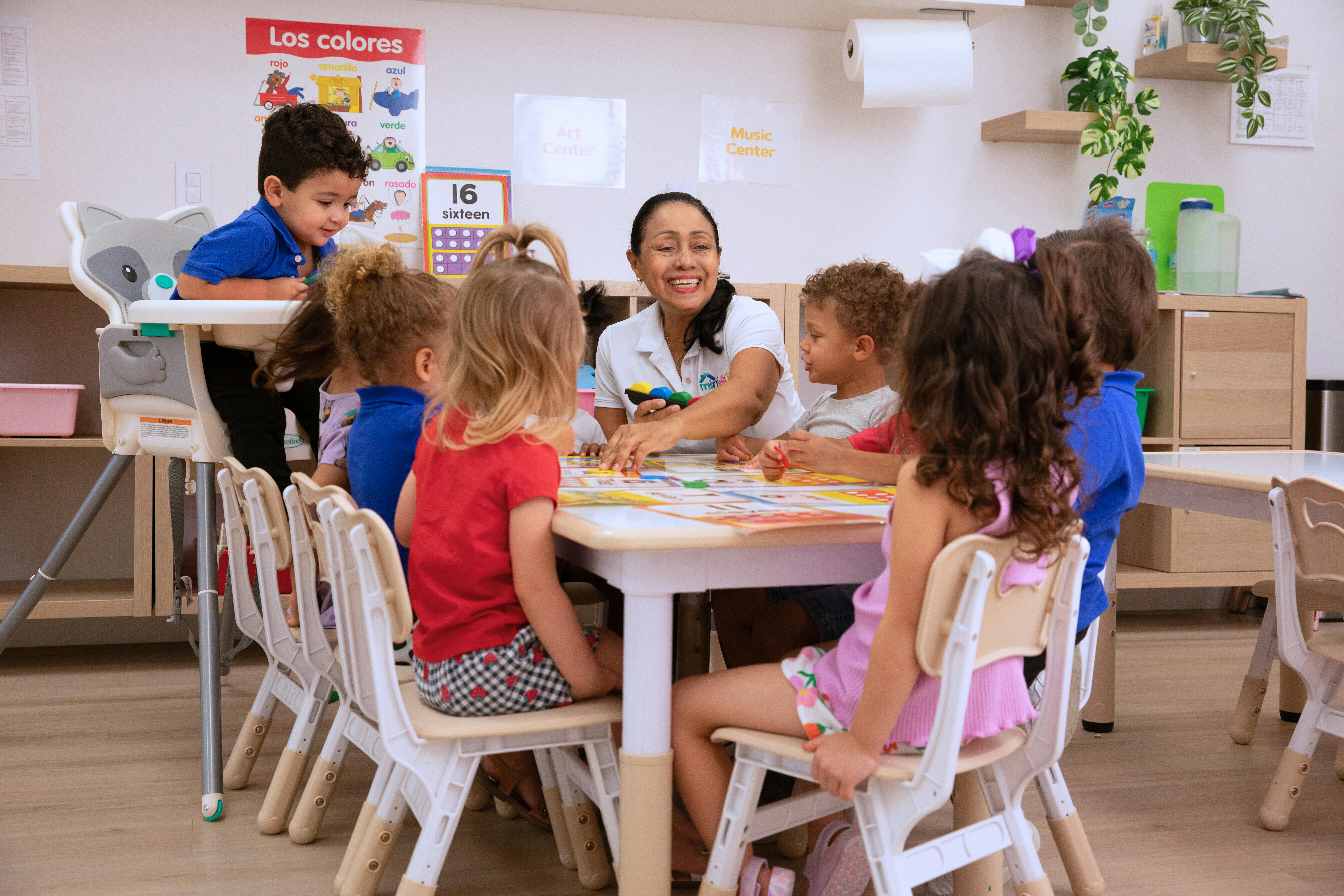 Teacher and young children sitting at a table in a classroom
