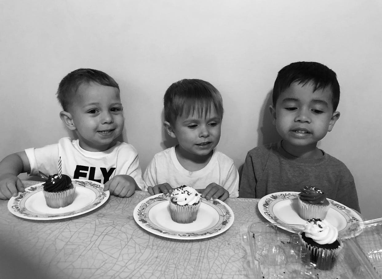 Three children sitting at a table with cupcakes