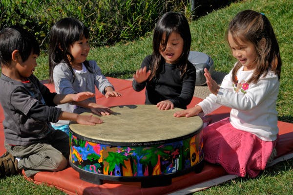 Four children playing a drum outdoors