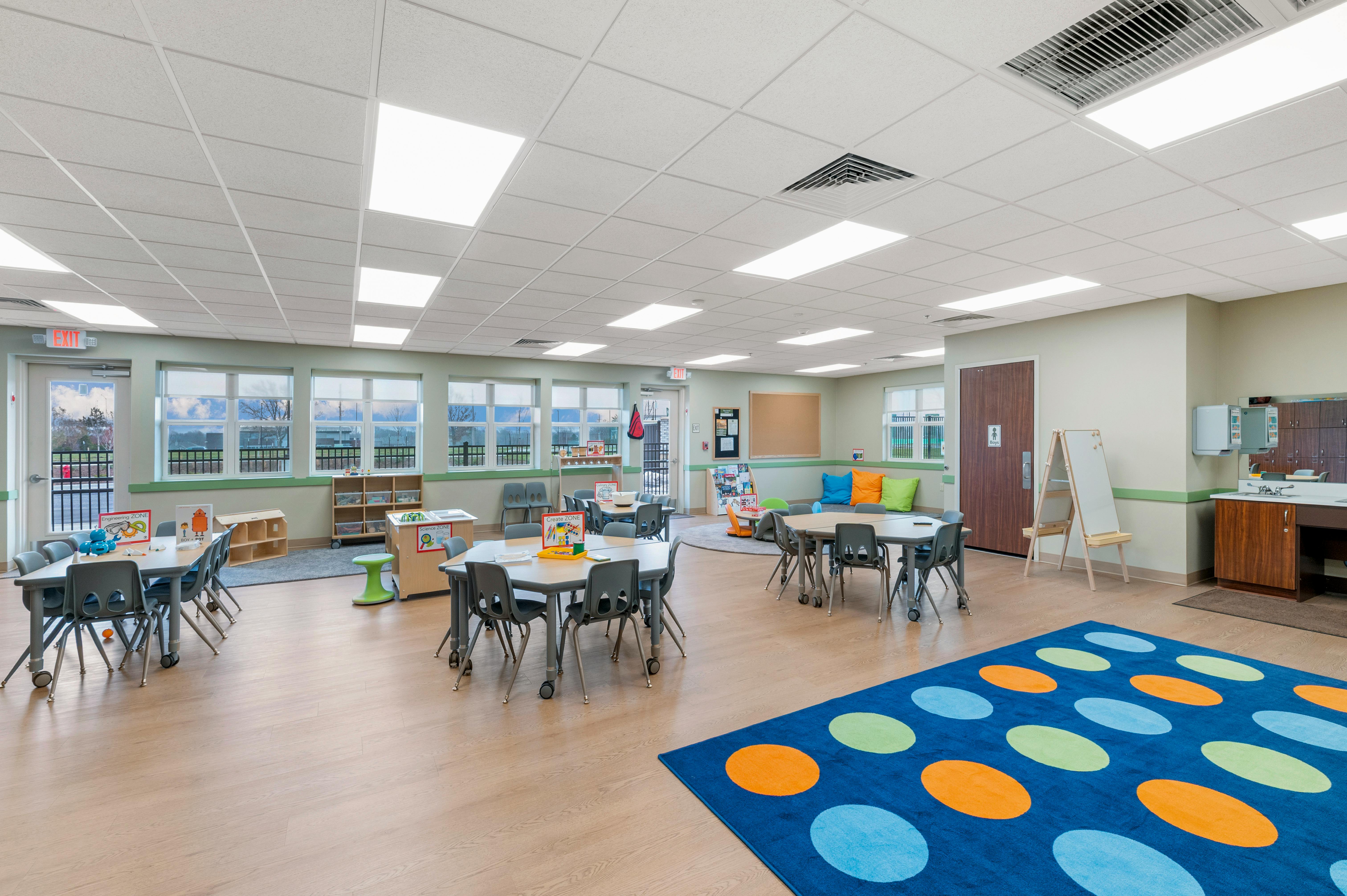 Classroom with multiple tables and chairs, windows, and a blue rug with circles