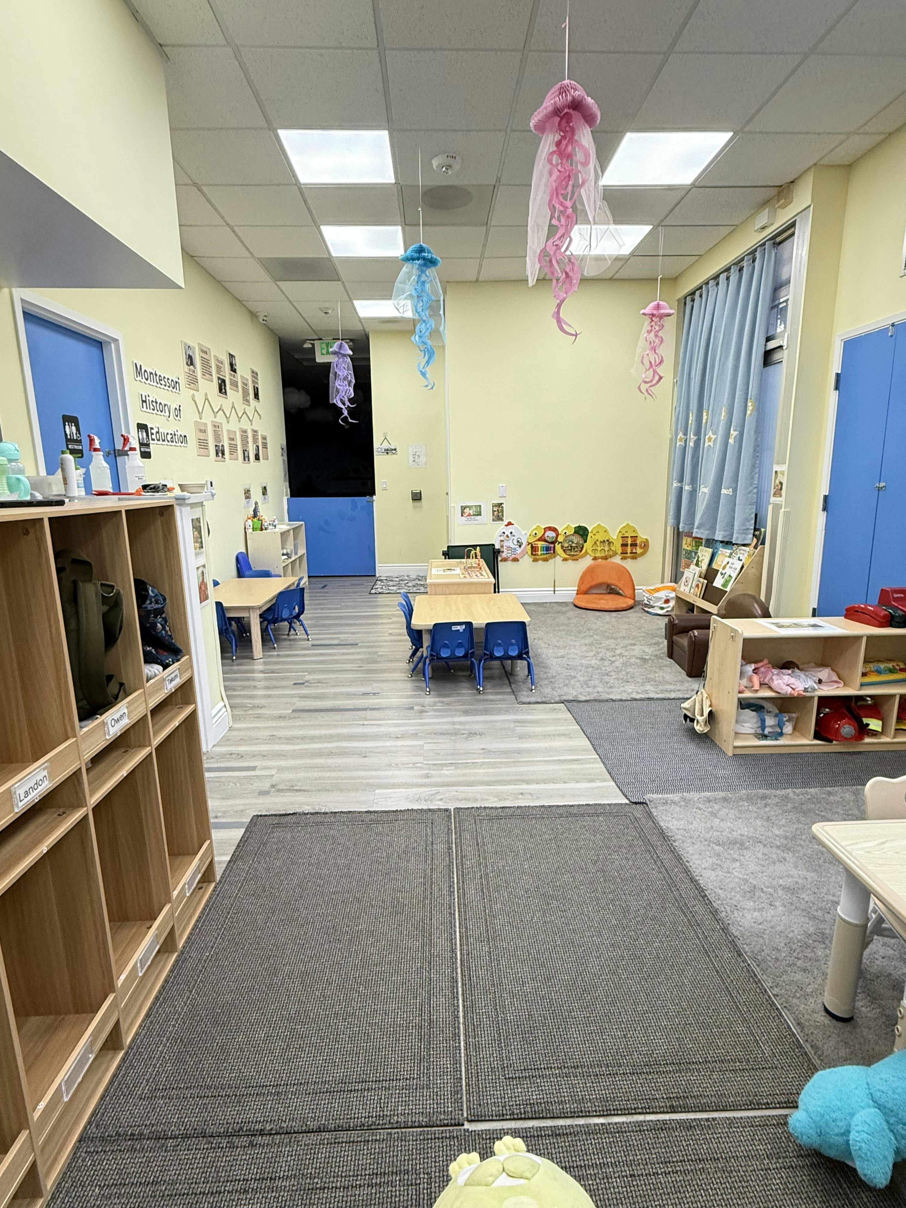Empty classroom with small tables and chairs, storage cubbies, and hanging decorations