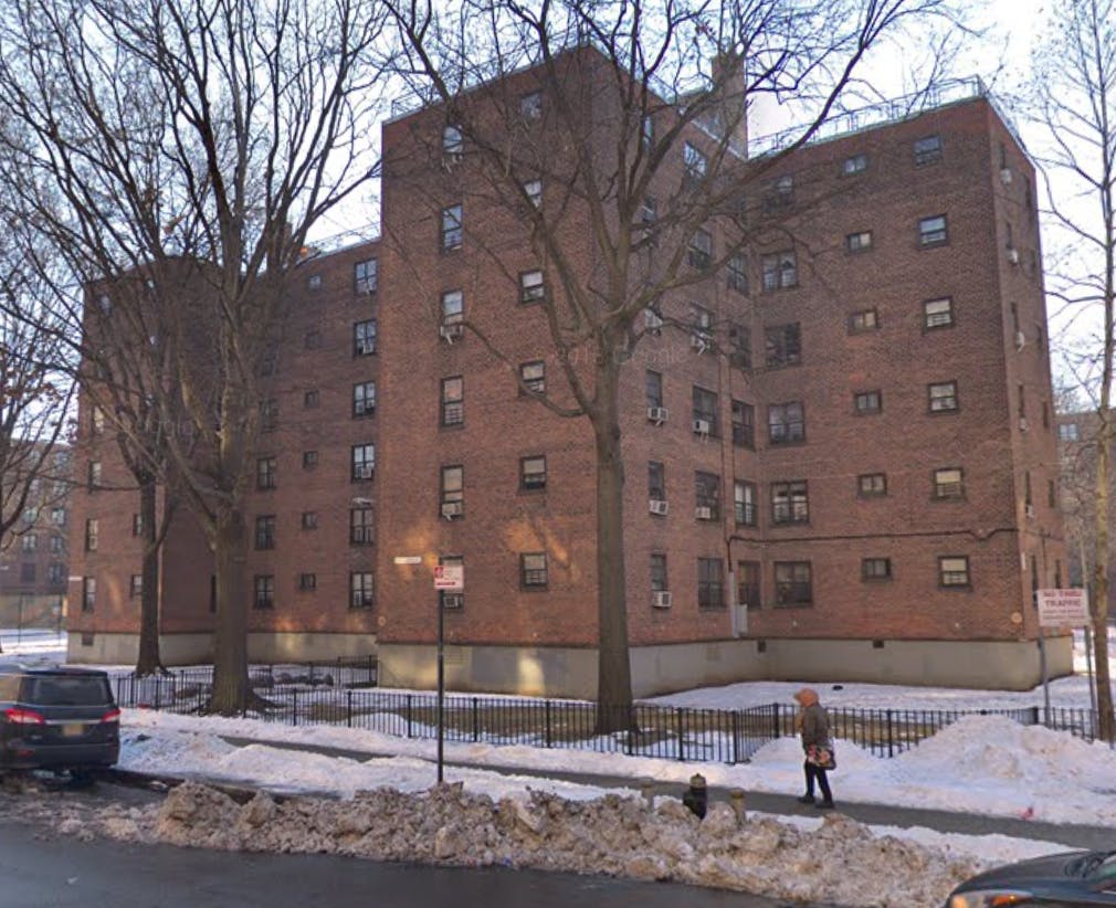 Large brick apartment building with bare trees and snow on the ground