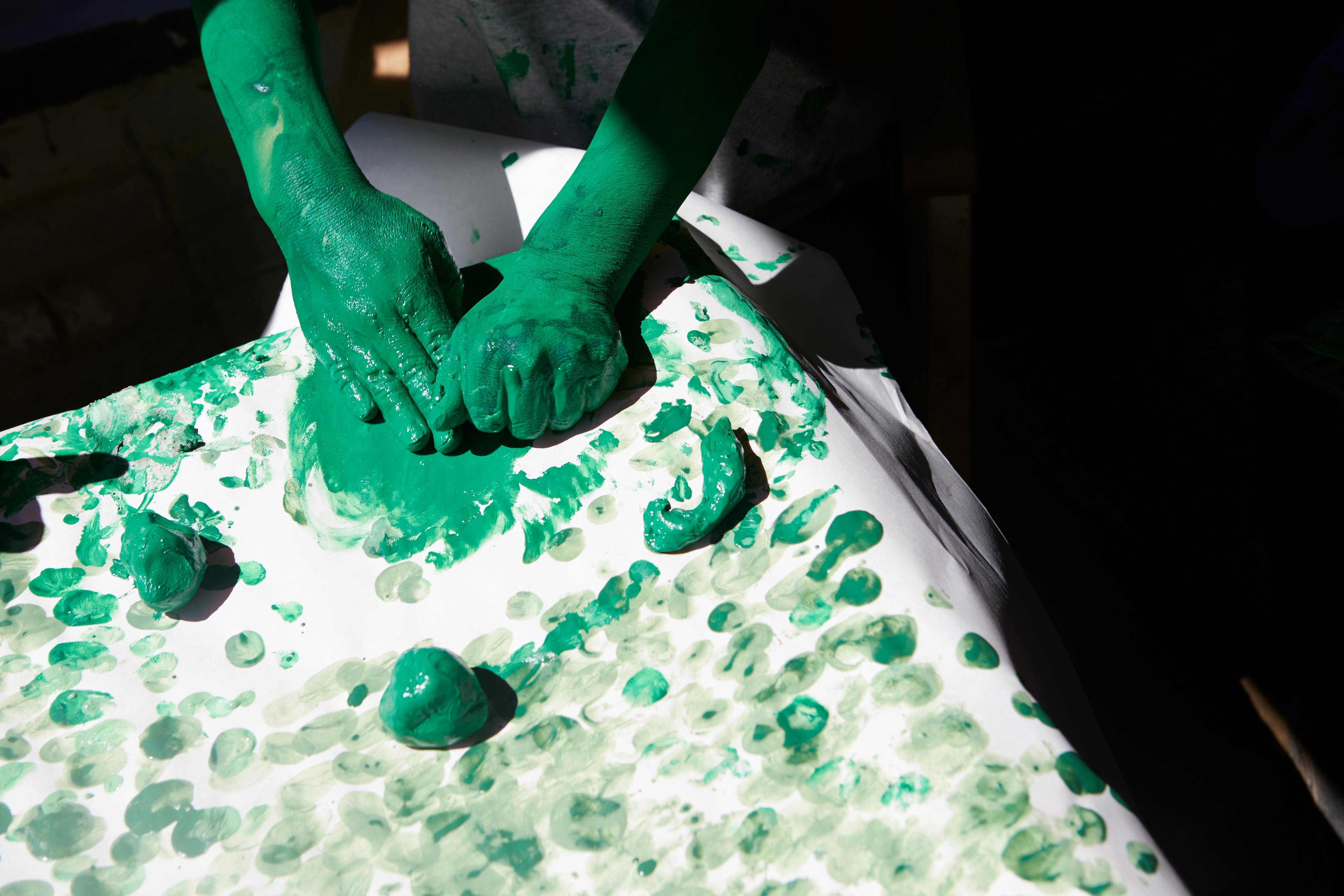 Person's hands covered in green paint pressing into a green substance