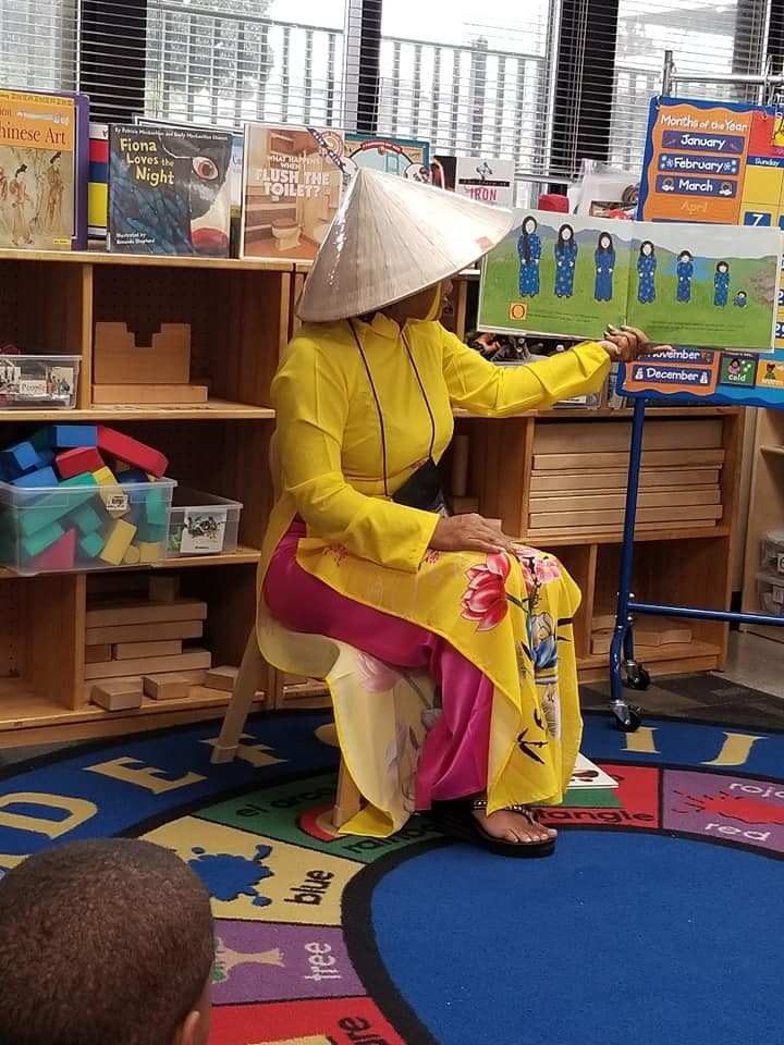 Person in conical hat and traditional clothing holding up a picture book