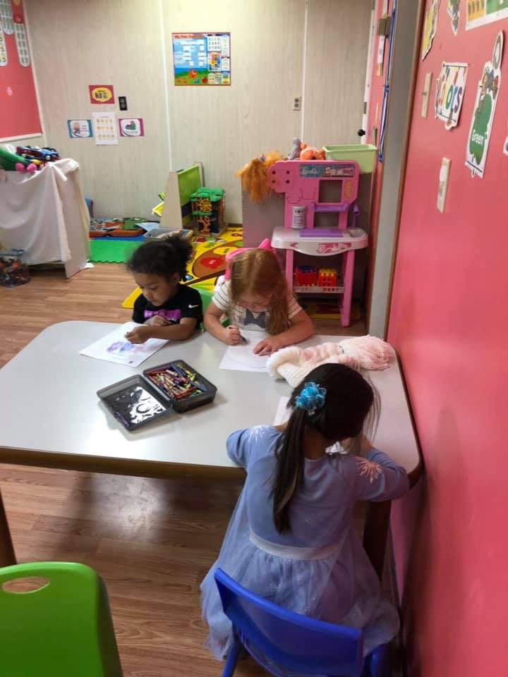 Three children drawing at a table in a classroom