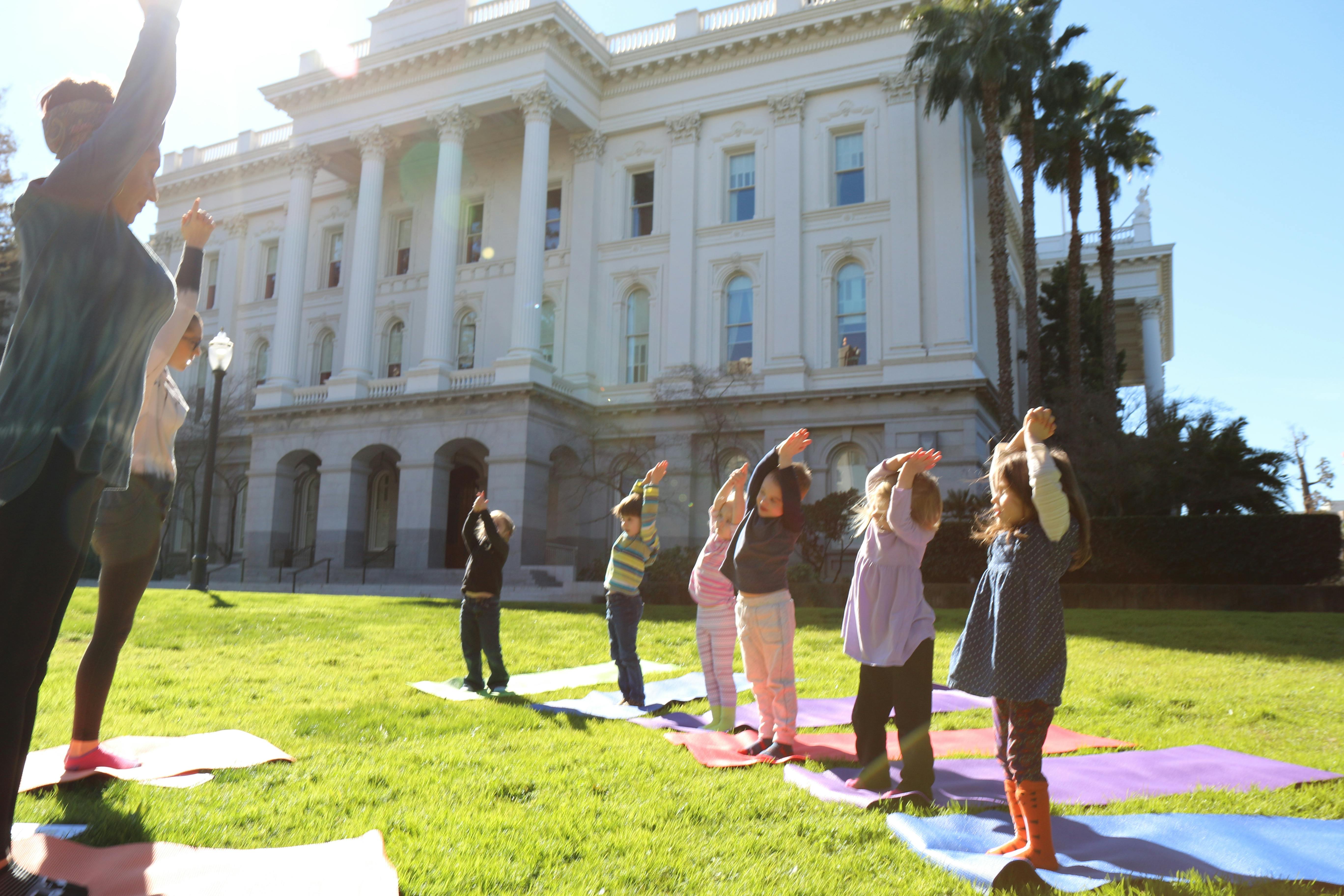 People and children doing yoga on mats in front of a large building