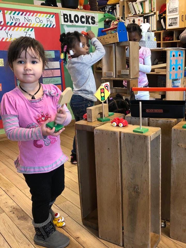 Child holding a toy paddle, other children playing with blocks in background