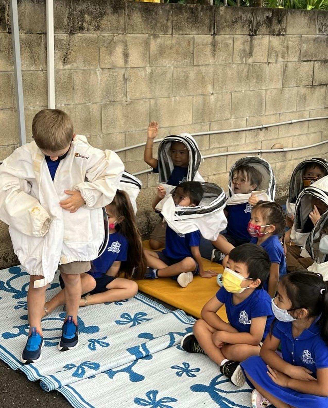 Child in white suit standing among other children in bee suits