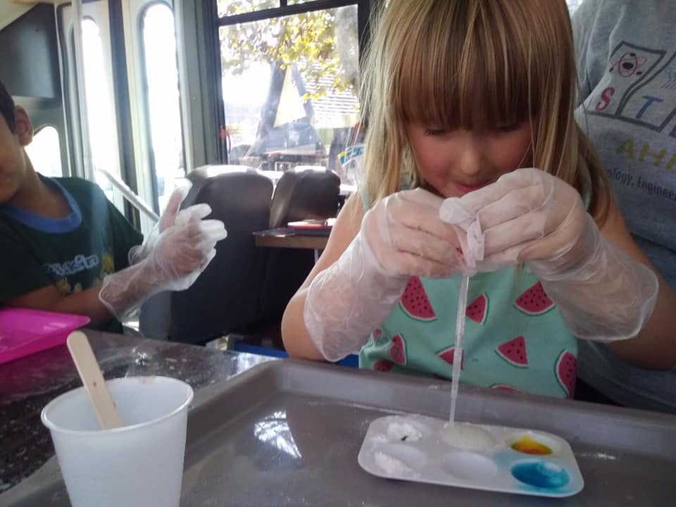 Child wearing gloves, mixing materials in a tray