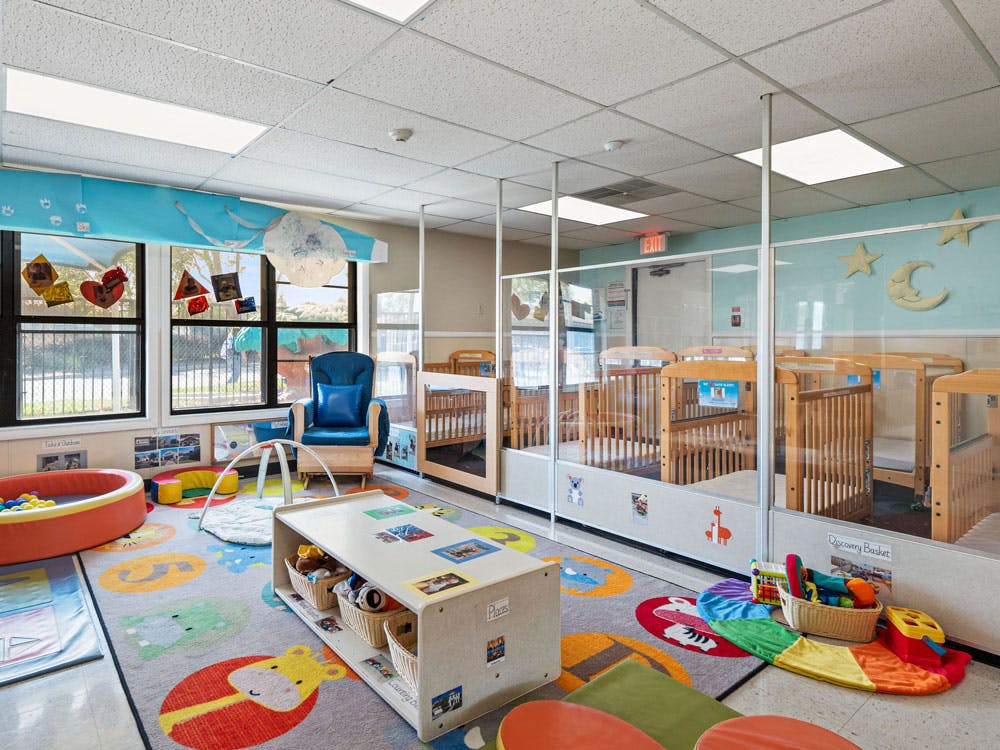 A colorful childcare room with cribs, play mats, and toys