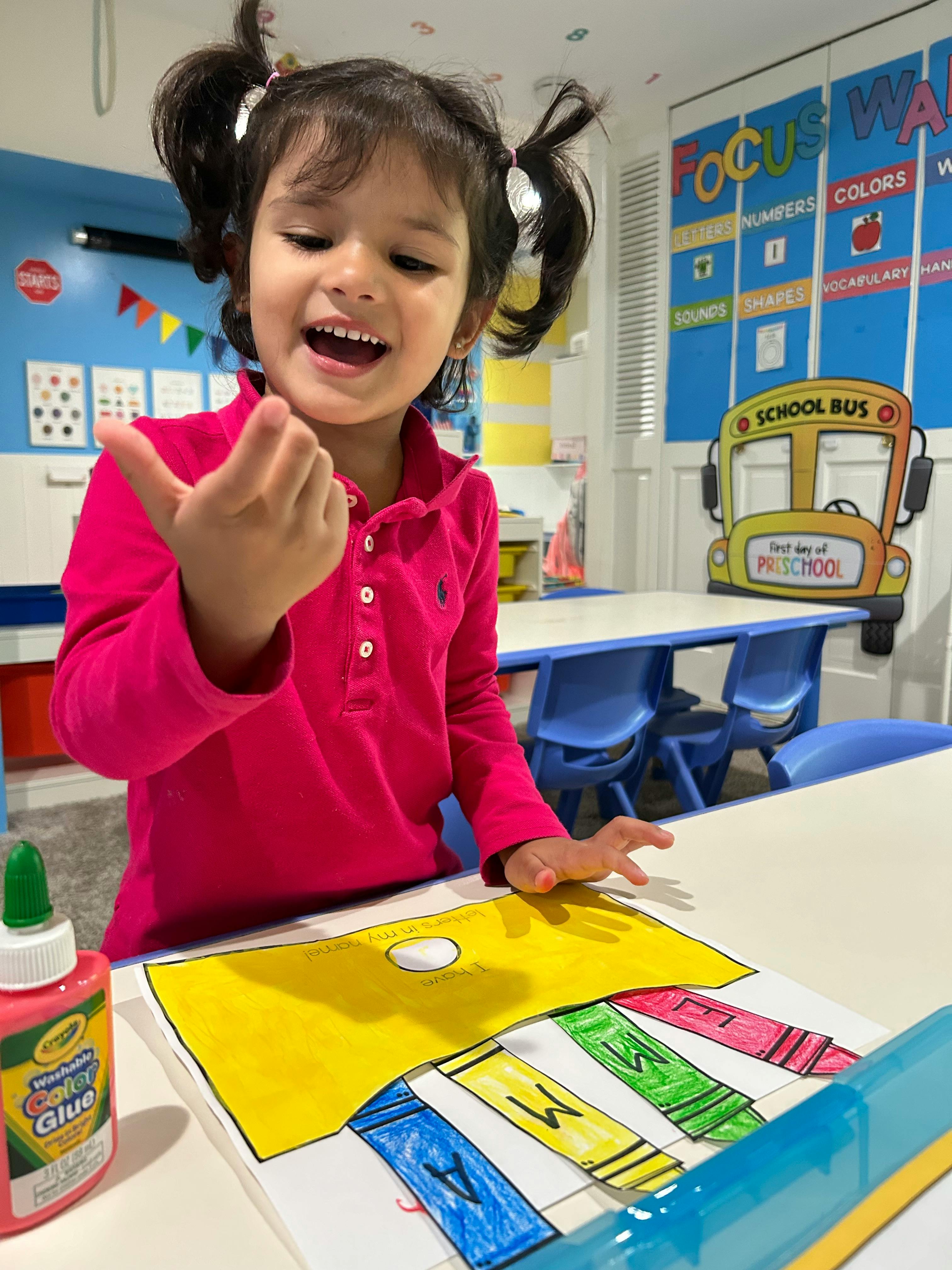 Child in a classroom with glue and a crayon drawing