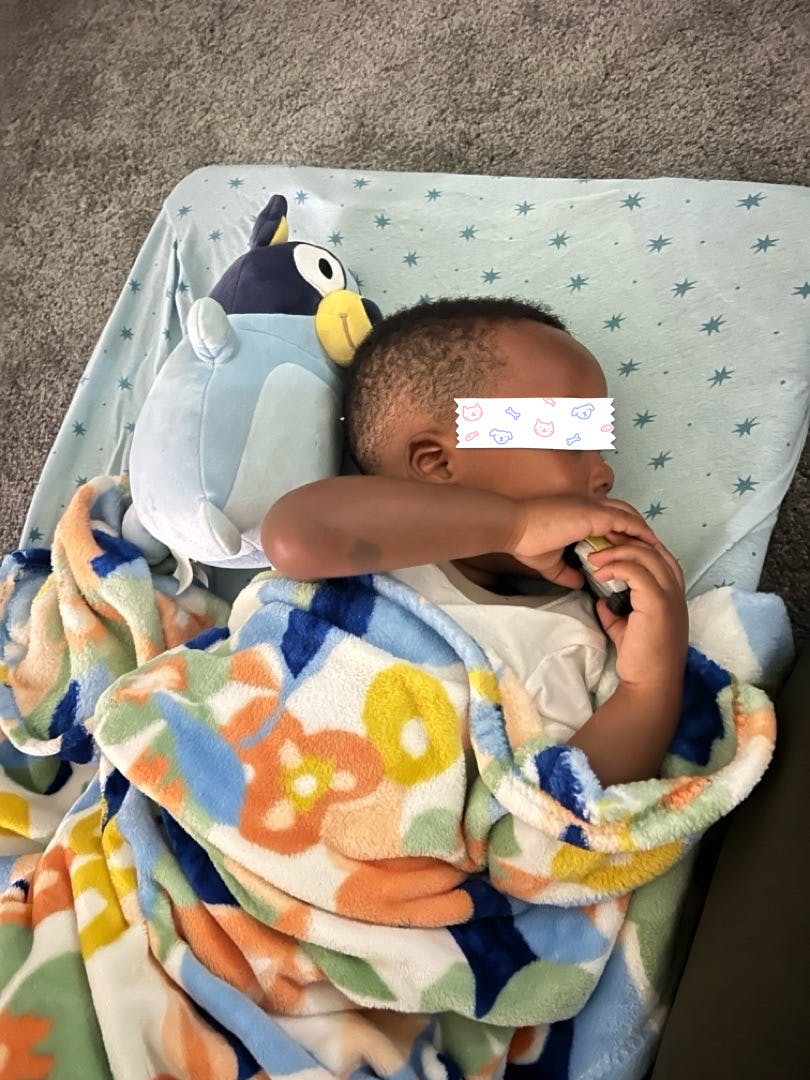 Child lying under a patterned blanket with a plush toy