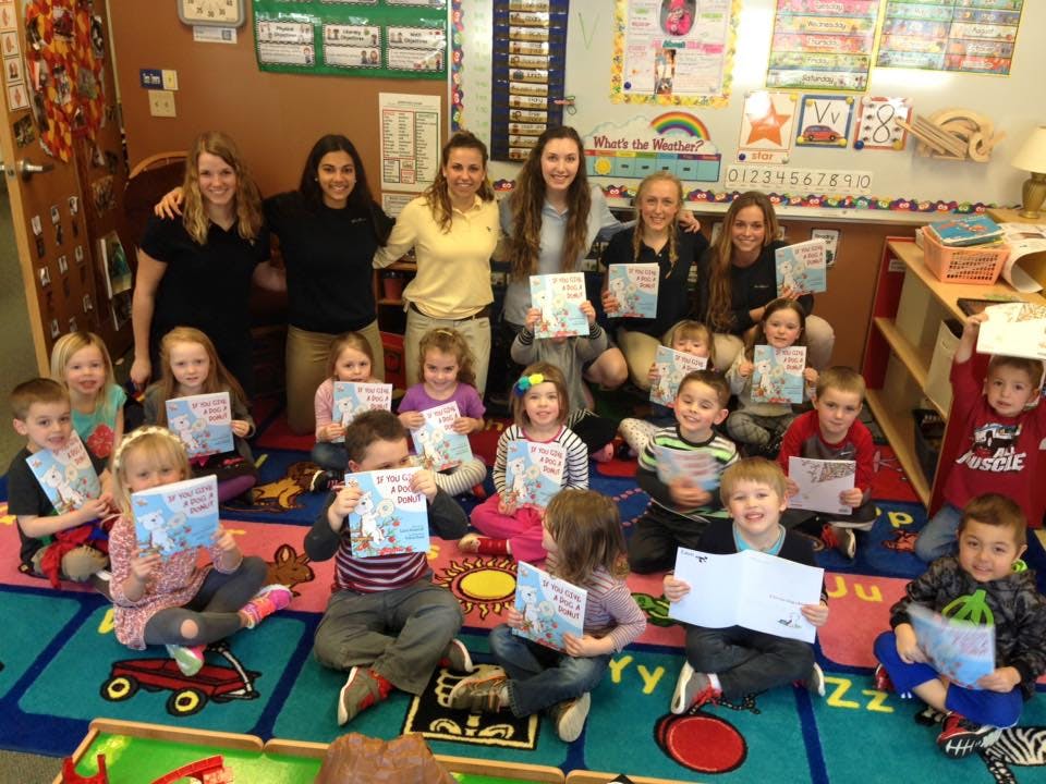 Adults and children holding books in a classroom