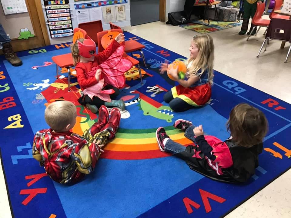 Four children sitting on a blue rug with a rainbow stripe