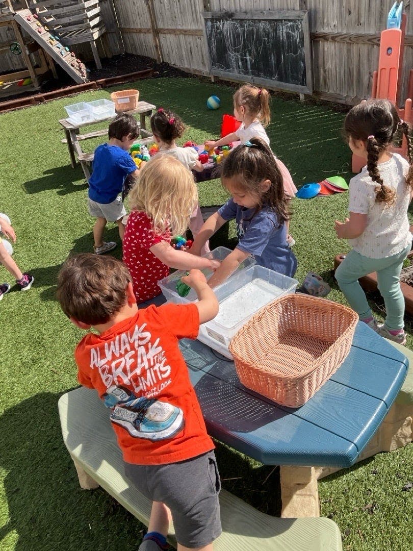 Group of children playing with water bins at a table outdoors