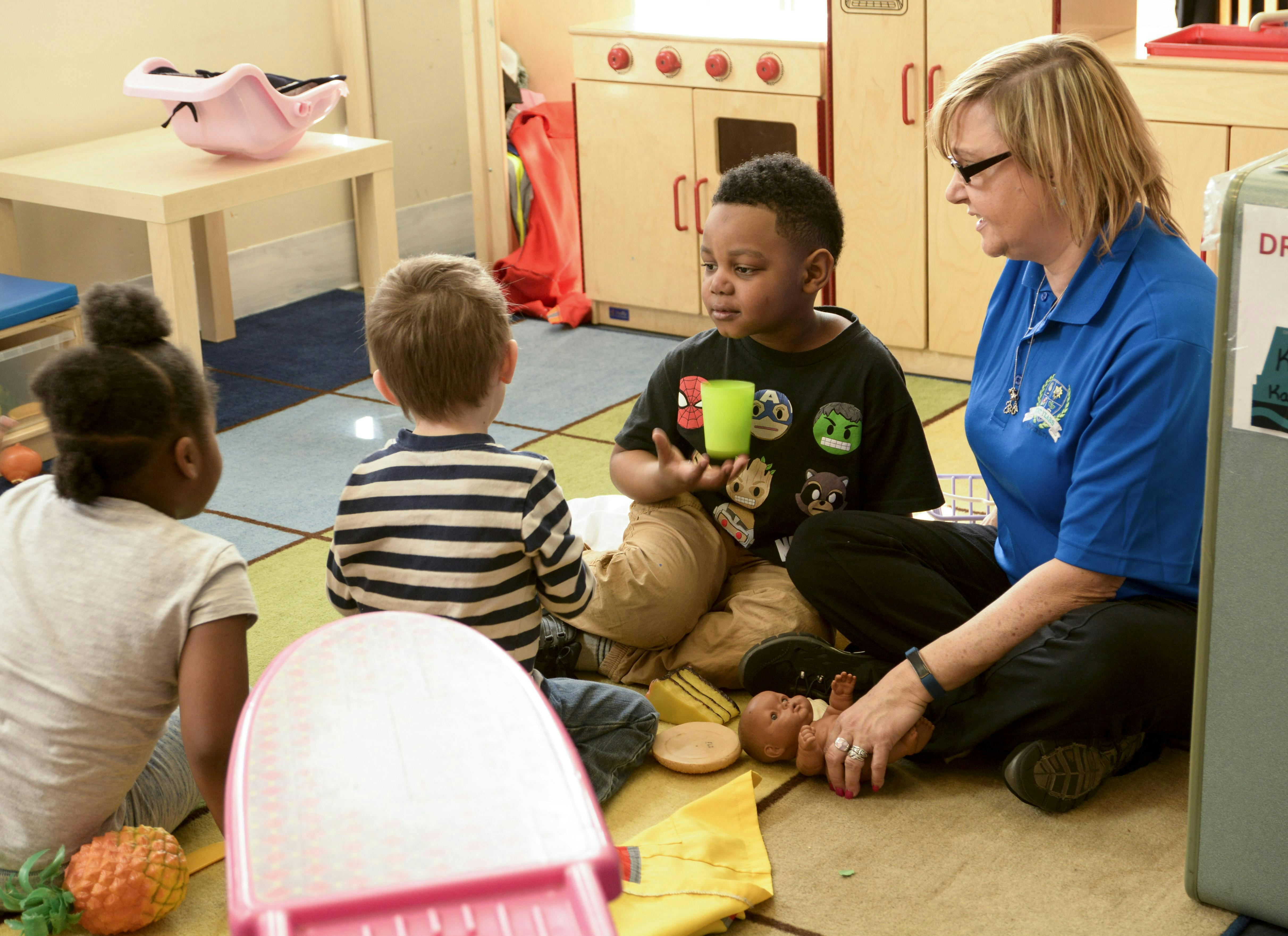 Adult and three children sitting on the floor in a classroom