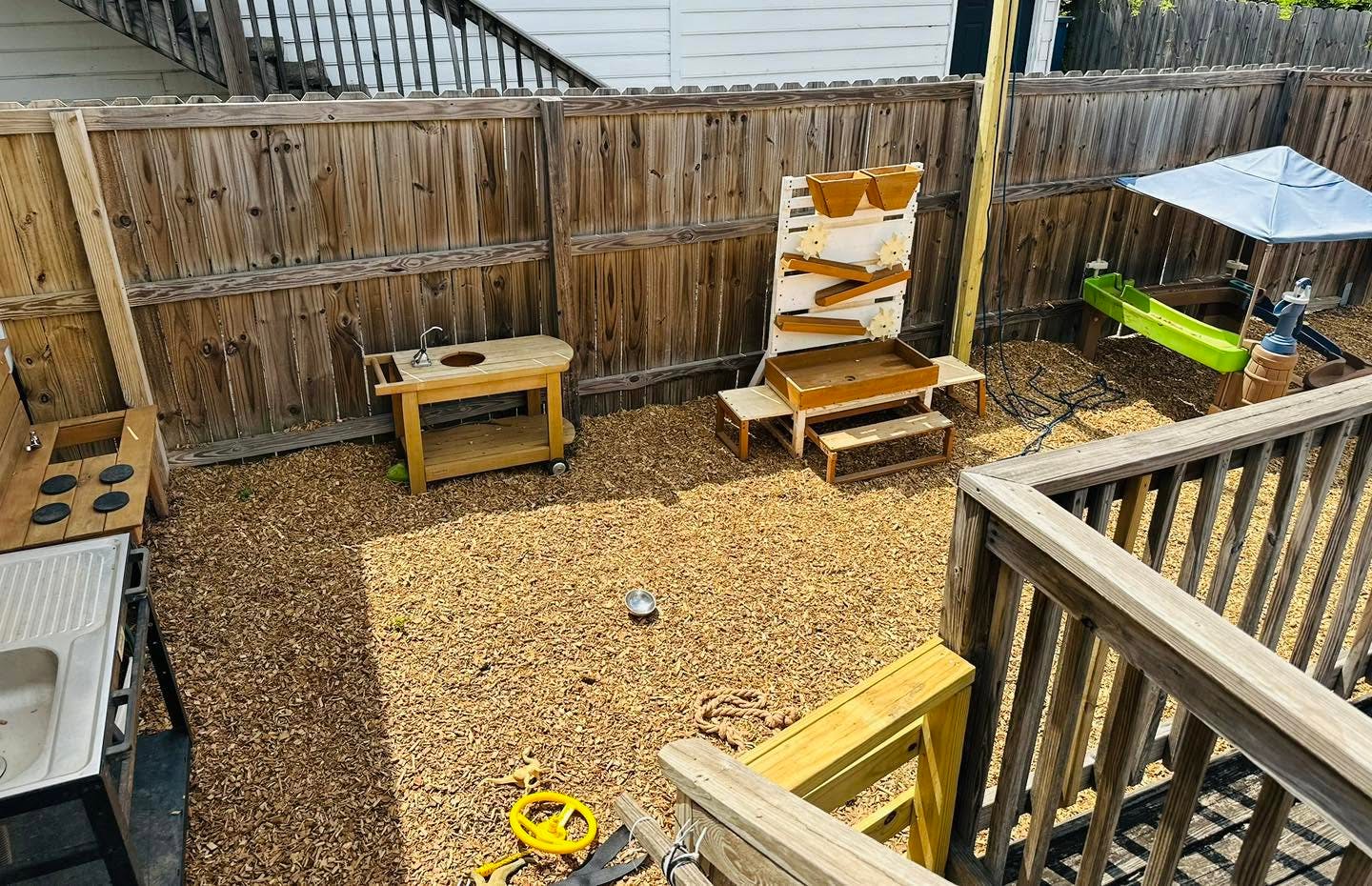 Wooden play area with sand and water stations in a fenced backyard