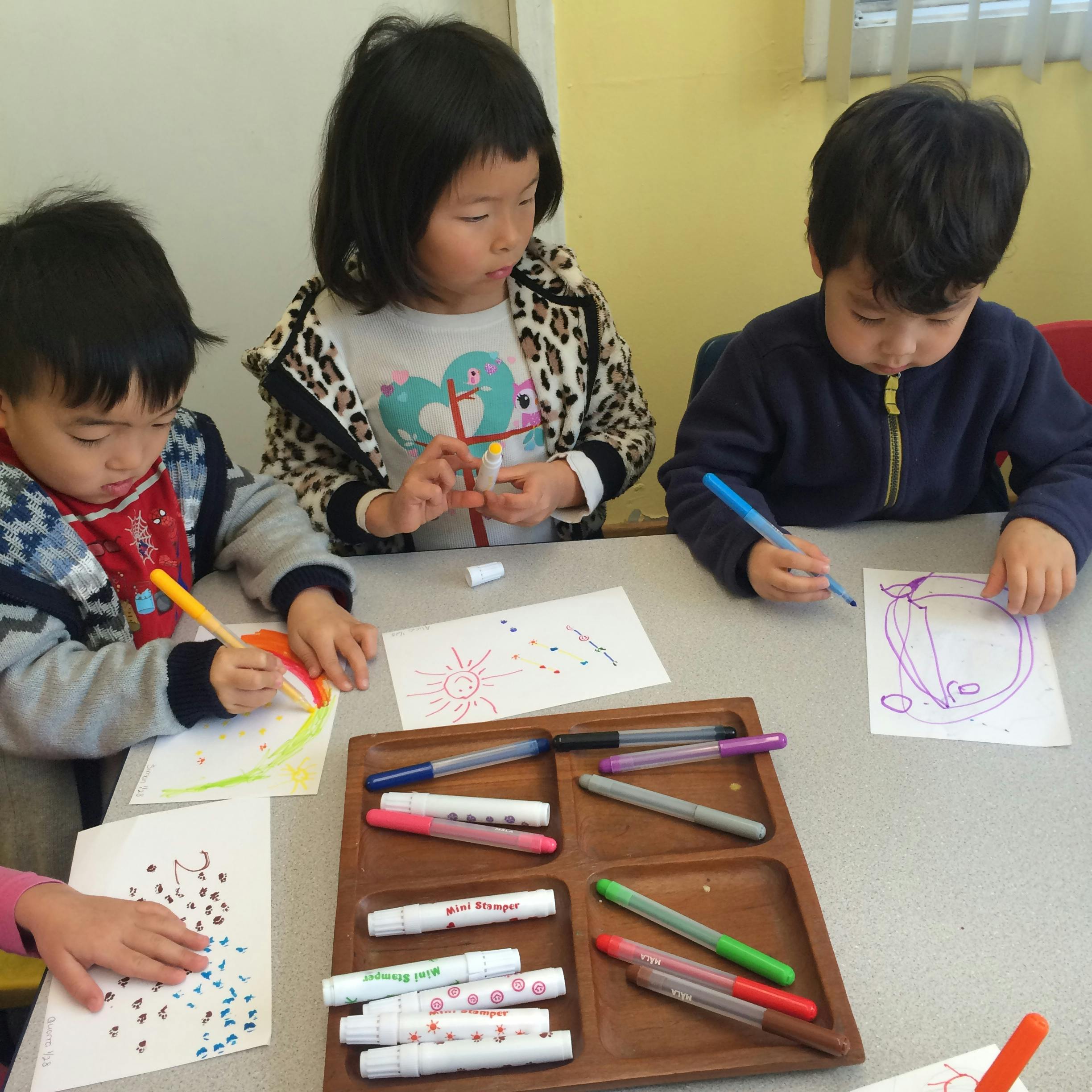 Three children drawing with markers at a table