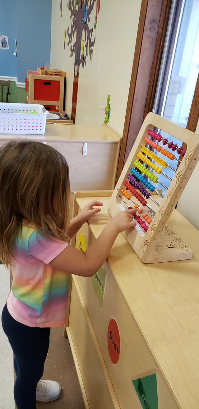 Child playing with a colorful abacus in a classroom