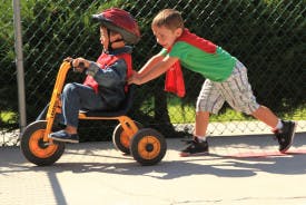 Child in helmet on tricycle being pushed by another child