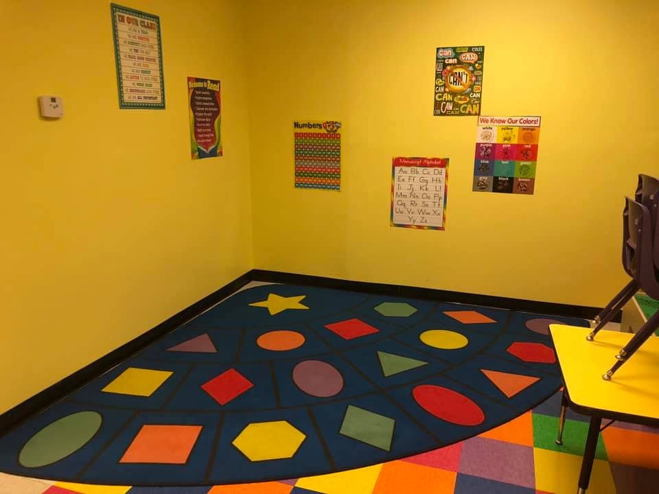 Classroom with yellow walls, colorful rug with shapes, and educational posters