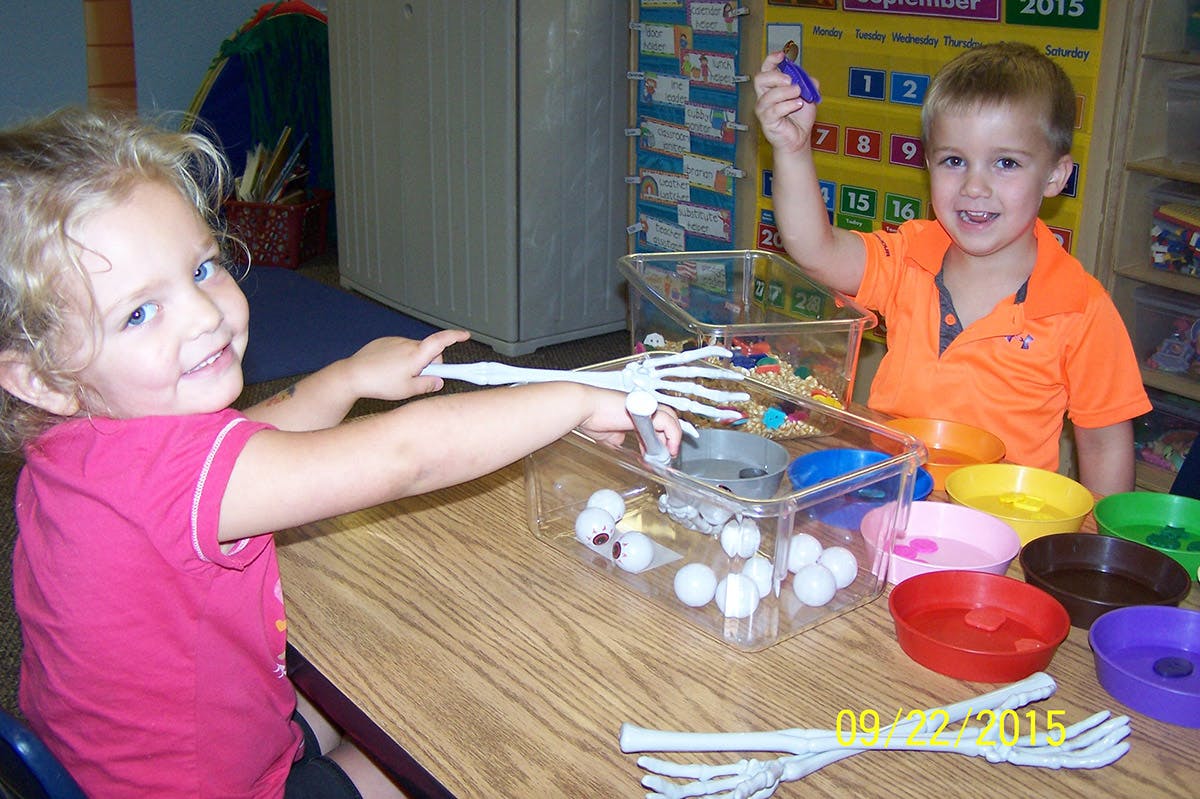 Two children playing with skeleton toys and colorful bowls at a table