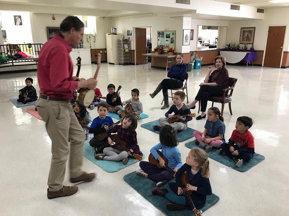 Person playing a banjo for a group of children with instruments