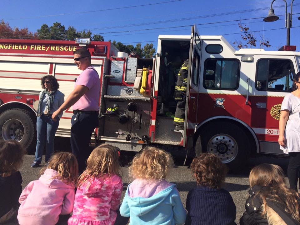 Children sitting on the ground in front of a fire truck with adults standing