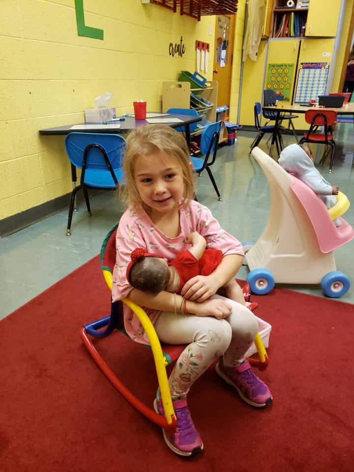 Child sitting in a chair holding a doll in a classroom