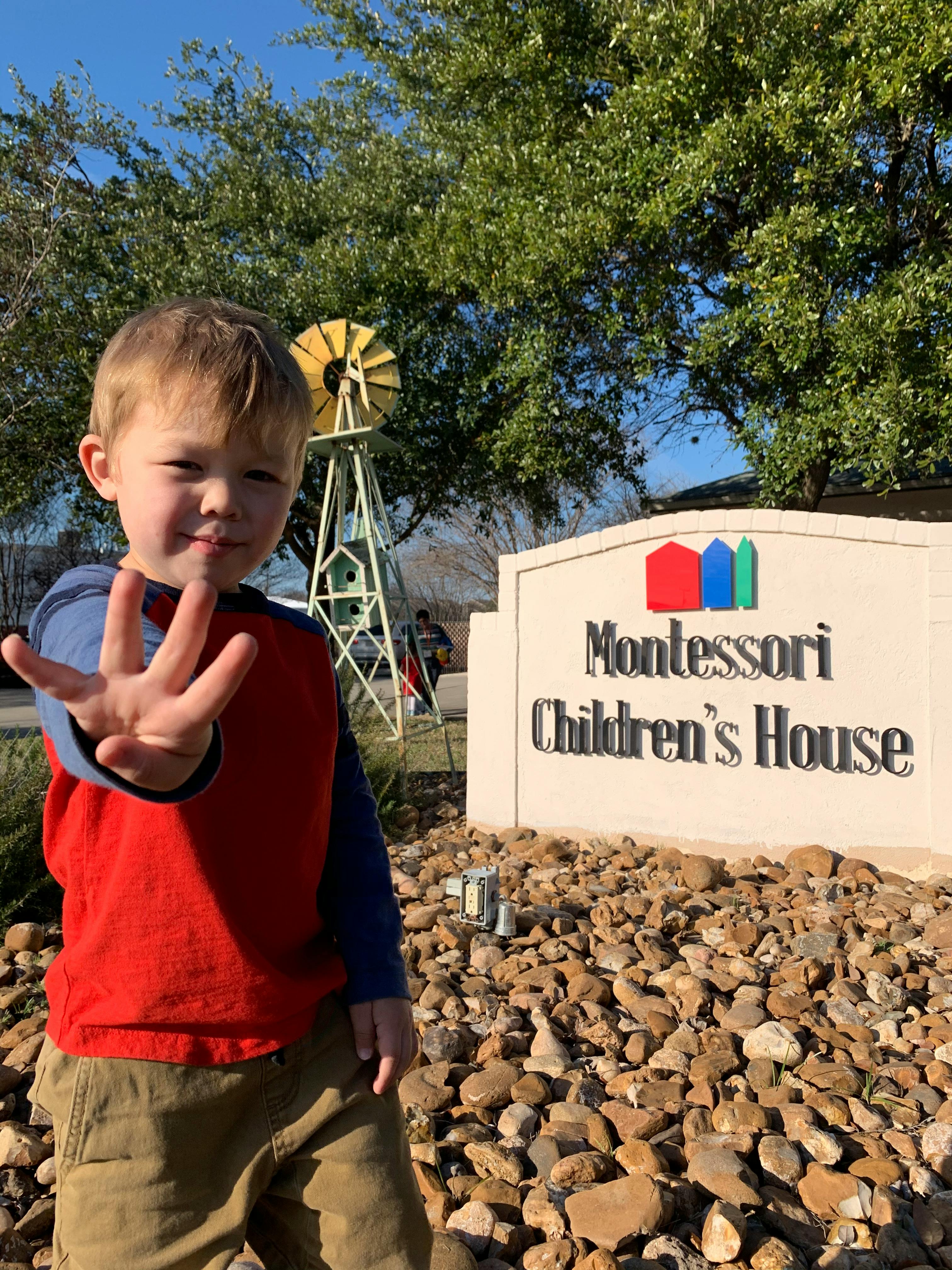 Child holding up hand in front of a Montessori Children's House sign