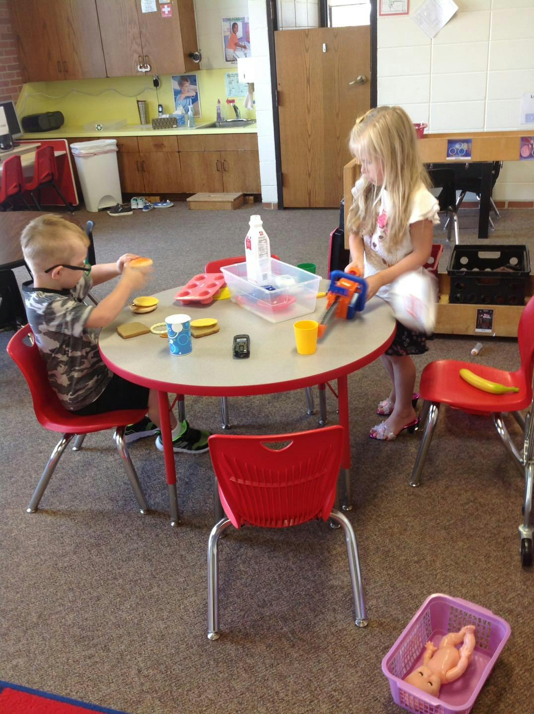 Two children playing with toys at a small round table in a classroom