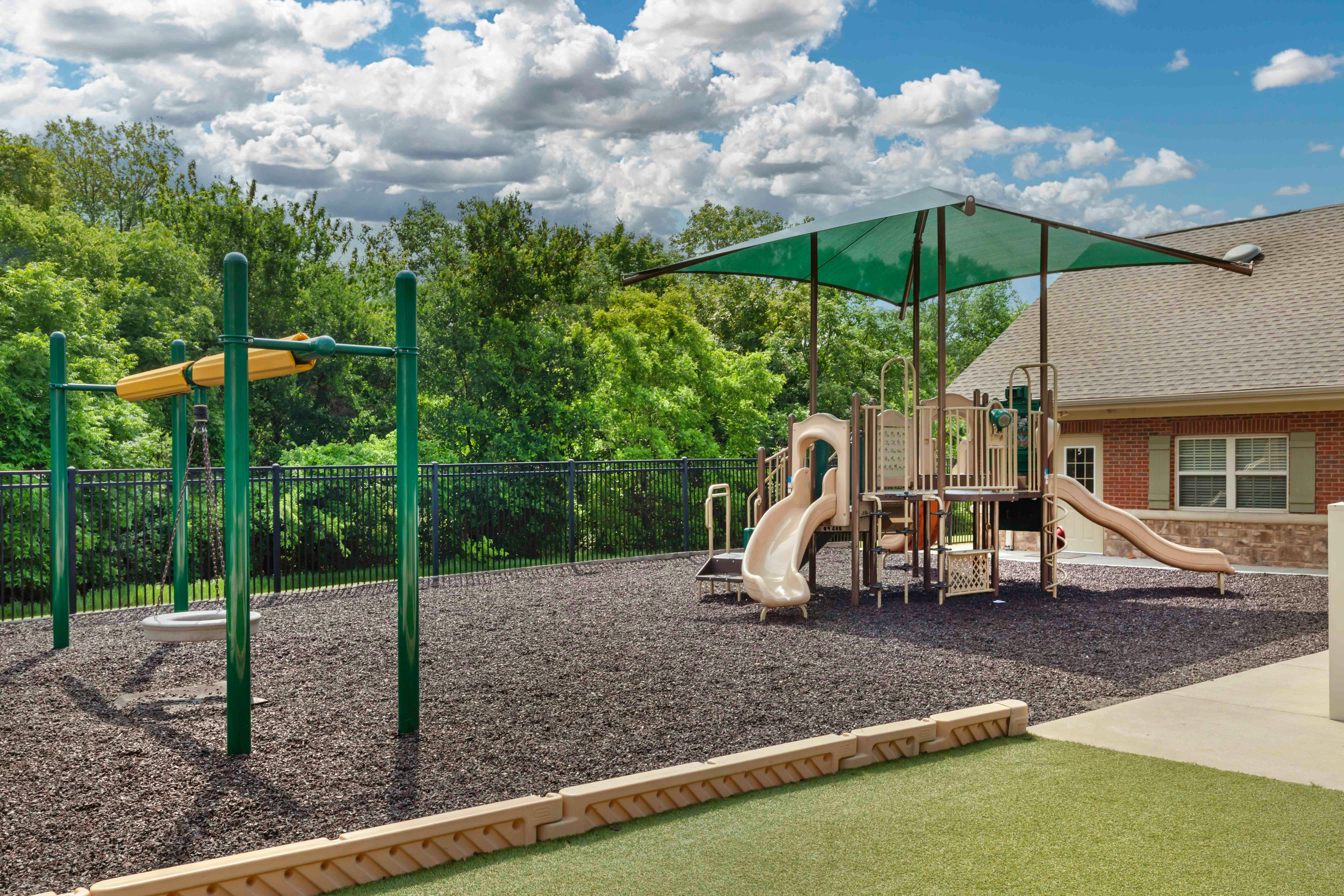Empty outdoor playground with slides, swings, and a green canopy over a structure