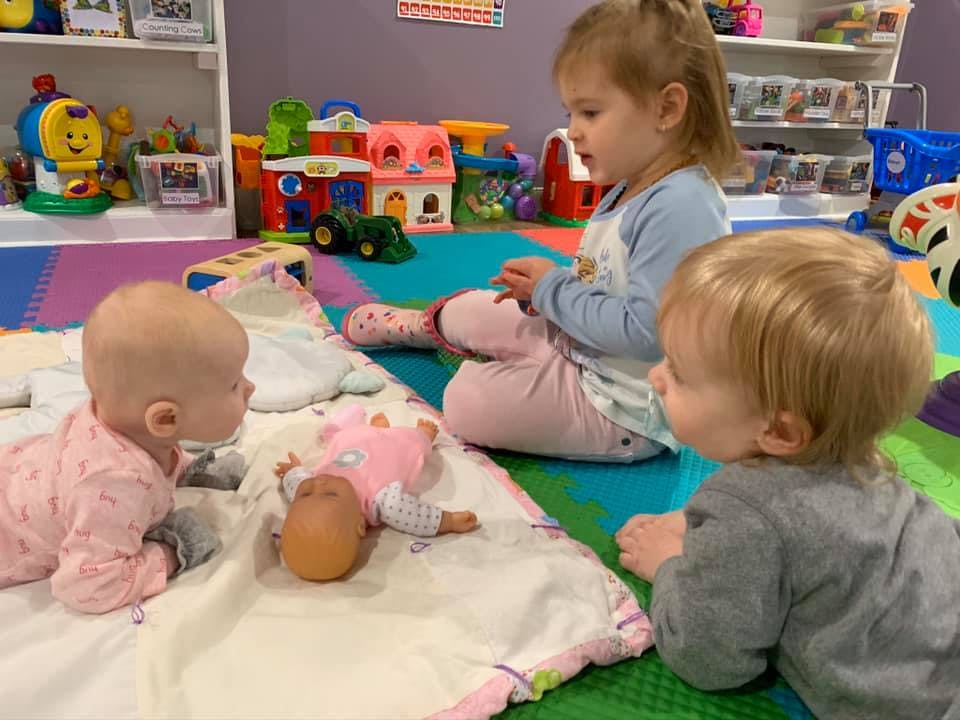 Three children playing with a doll on a mat